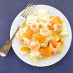 sauteed cabbage with shrimp on white plate with fork.